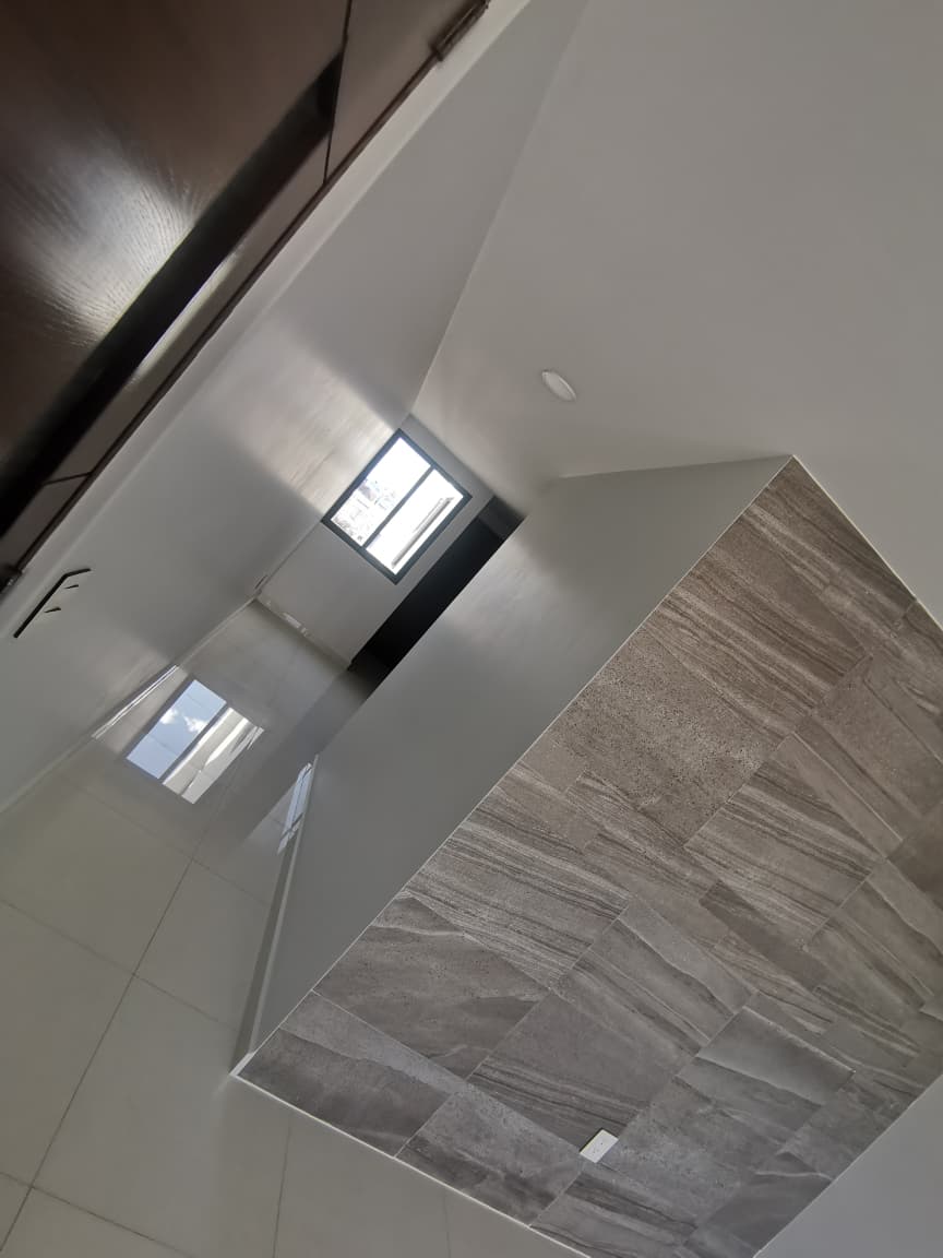Pasillo iluminado con piso de cerámica y detalle de pared de azulejo.