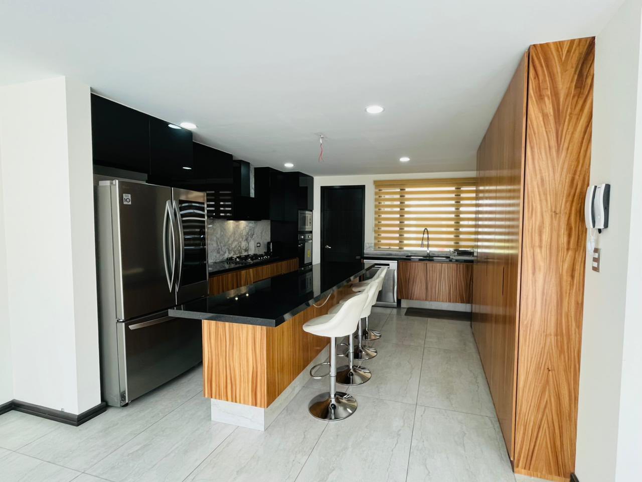 Cocina integral con isla central, acabados en granito y madera, equipada con electrodomésticos modernos.