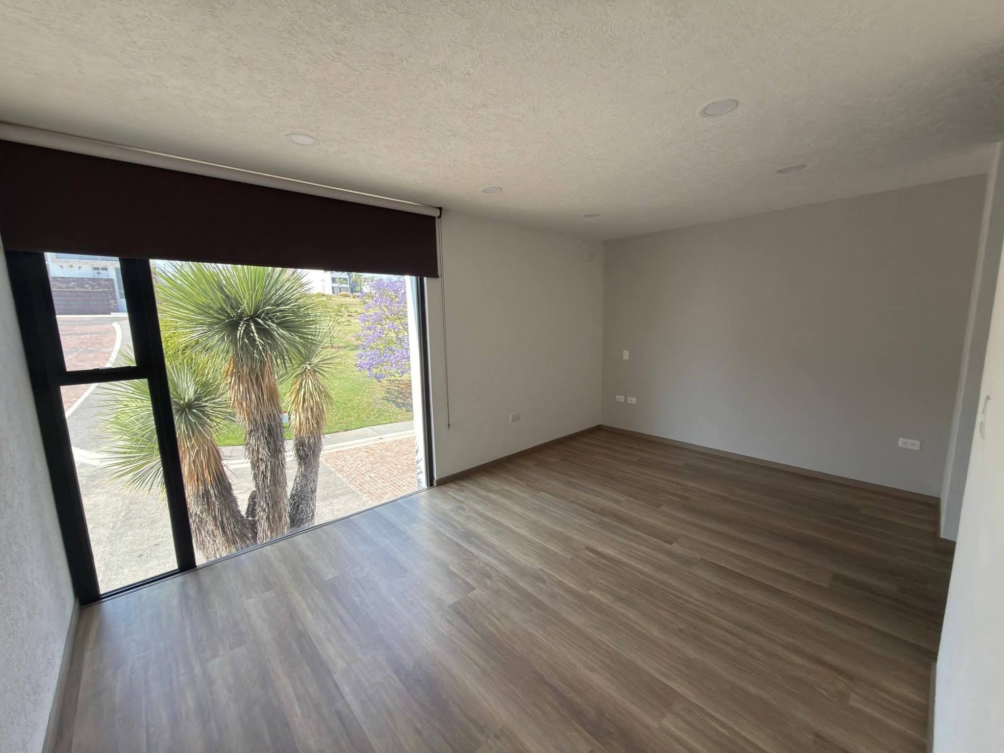 Amplia recámara con piso de madera y gran ventanal con vista al exterior.