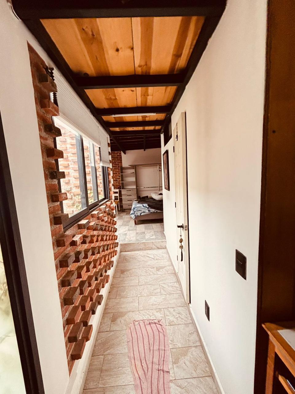 Pasillo con techo de vigas de madera y vista a la recámara, conecta diferentes espacios.