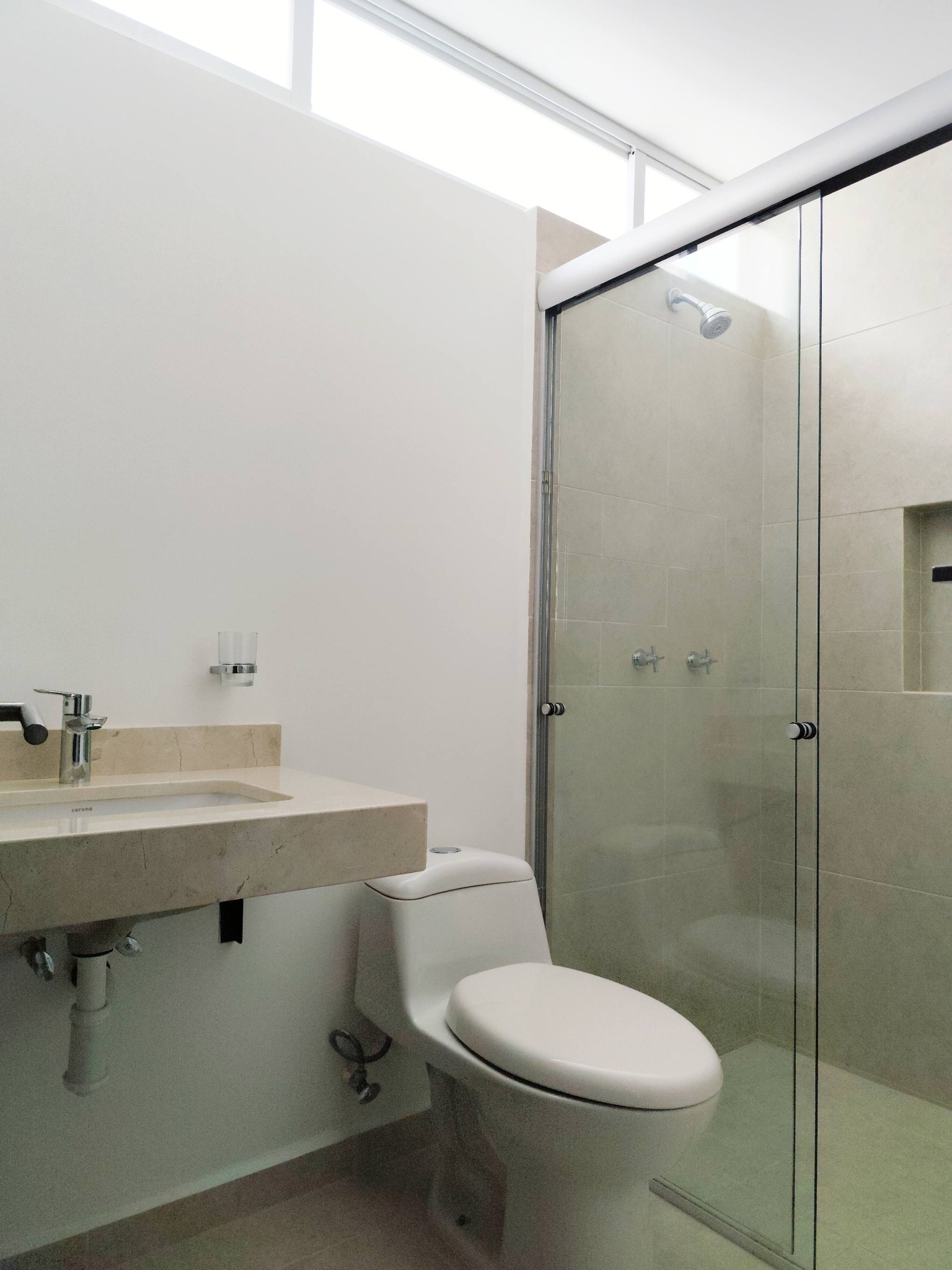 Baño con ducha de cristal y acabados en mármol claro.