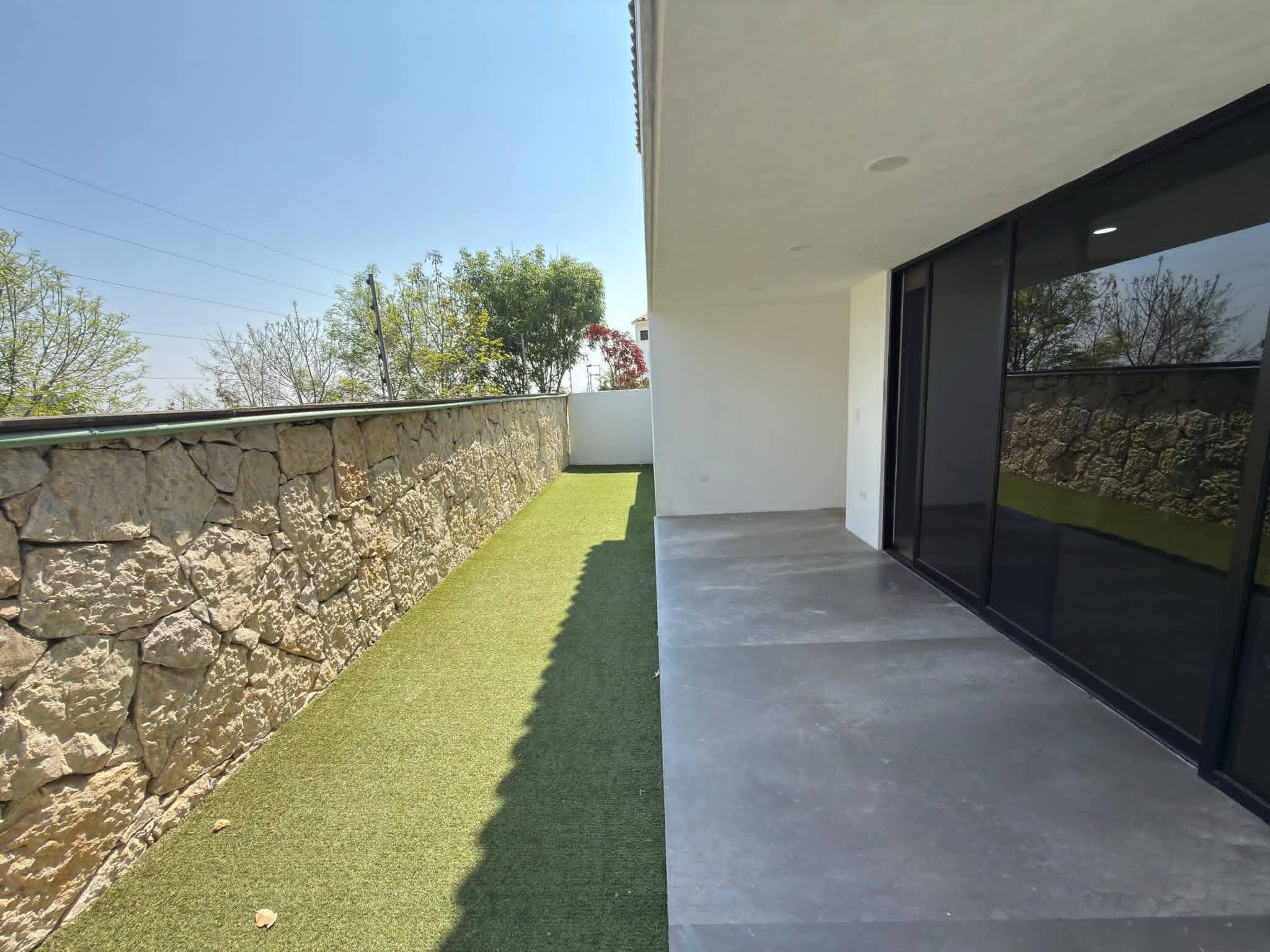 Área de jardín con césped sintético y muro de piedra.
