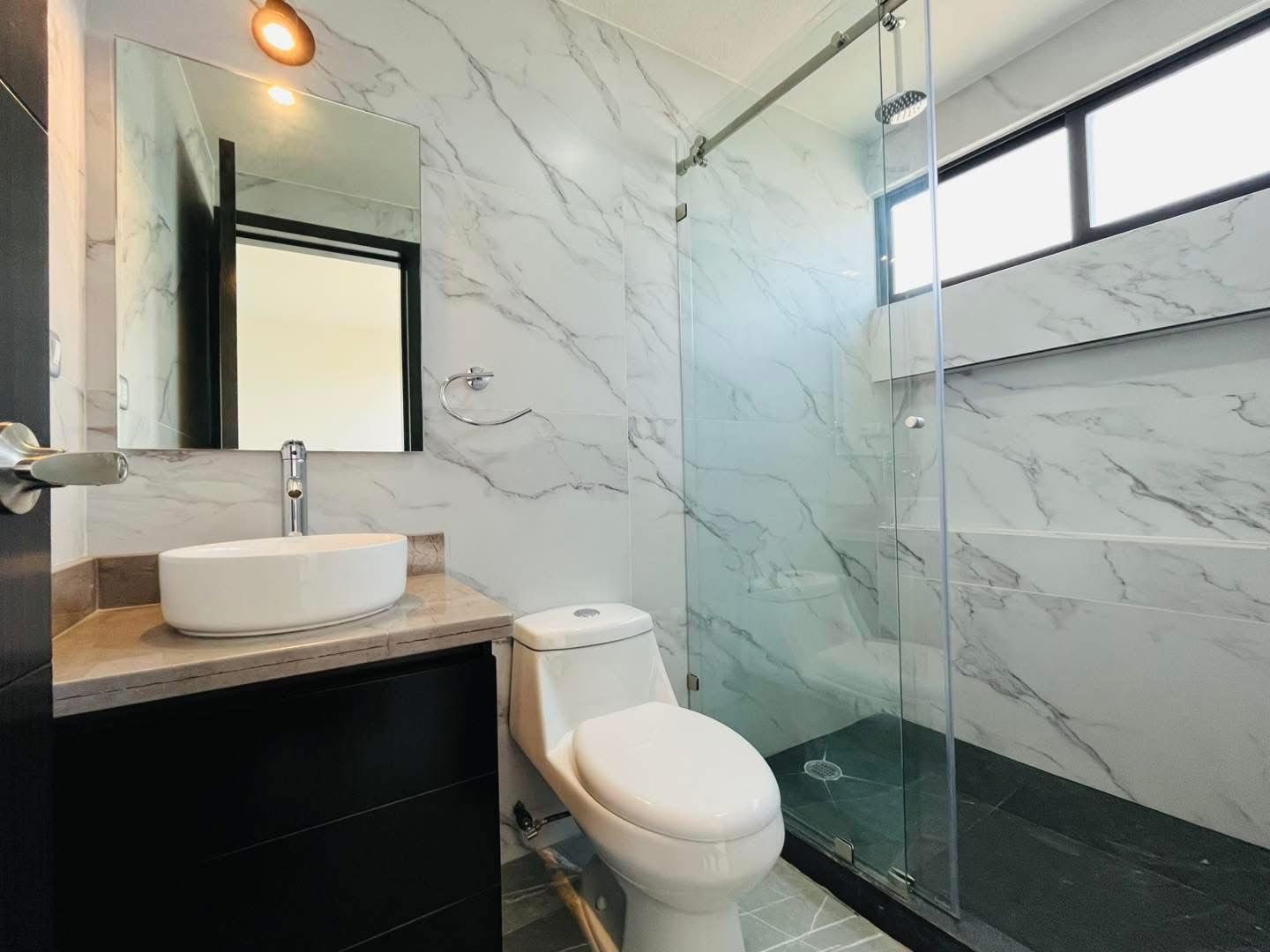 Baño elegante con mármol, doble lavabo y ducha de cristal.