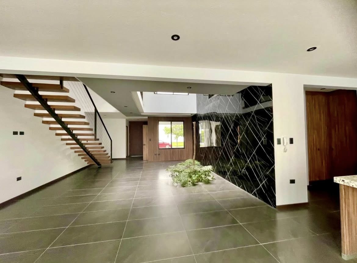 Amplia sala con un muro de mármol negro y escalera flotante de madera.
