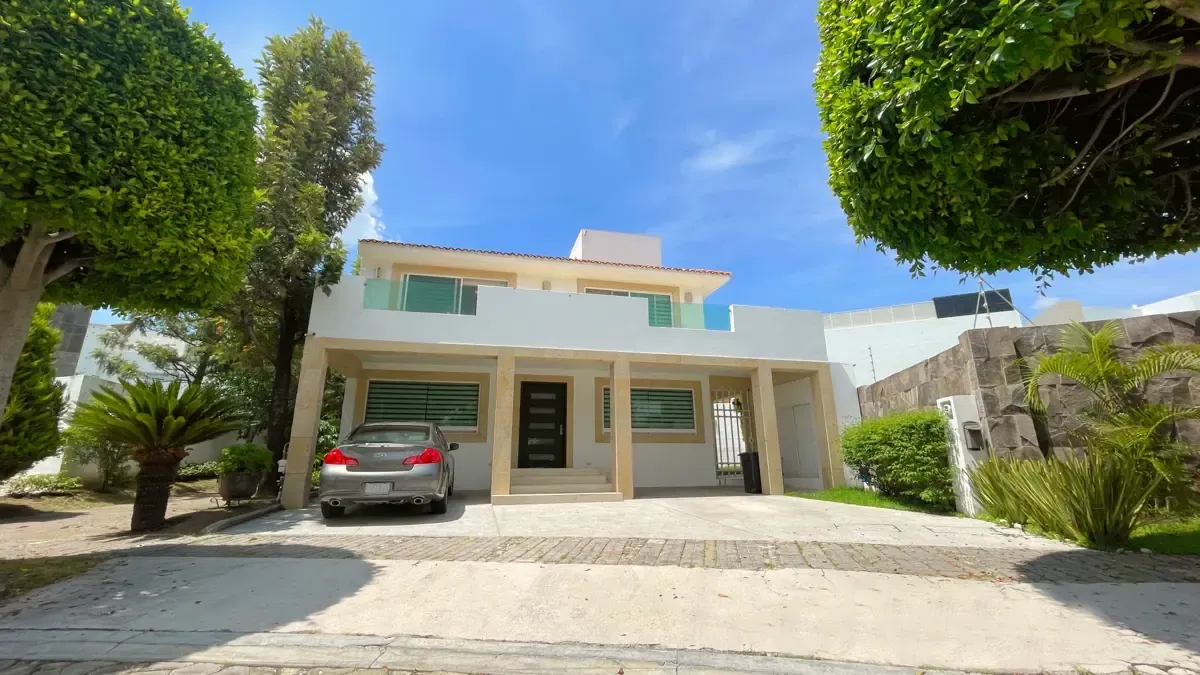 Fachada de la casa con estacionamiento techado y jardín frontal.