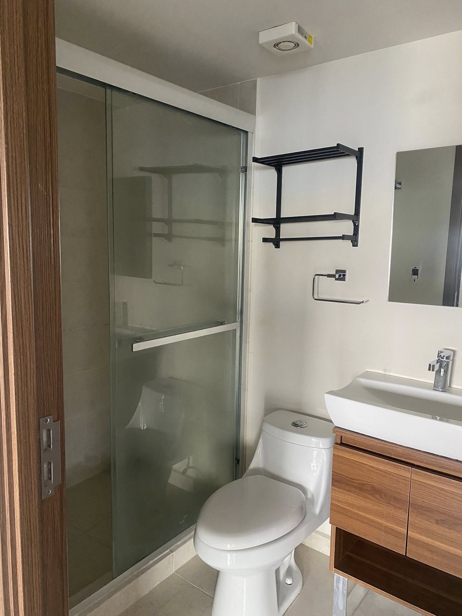 Baño moderno con ducha de vidrio templado y mueble de lavabo de madera.