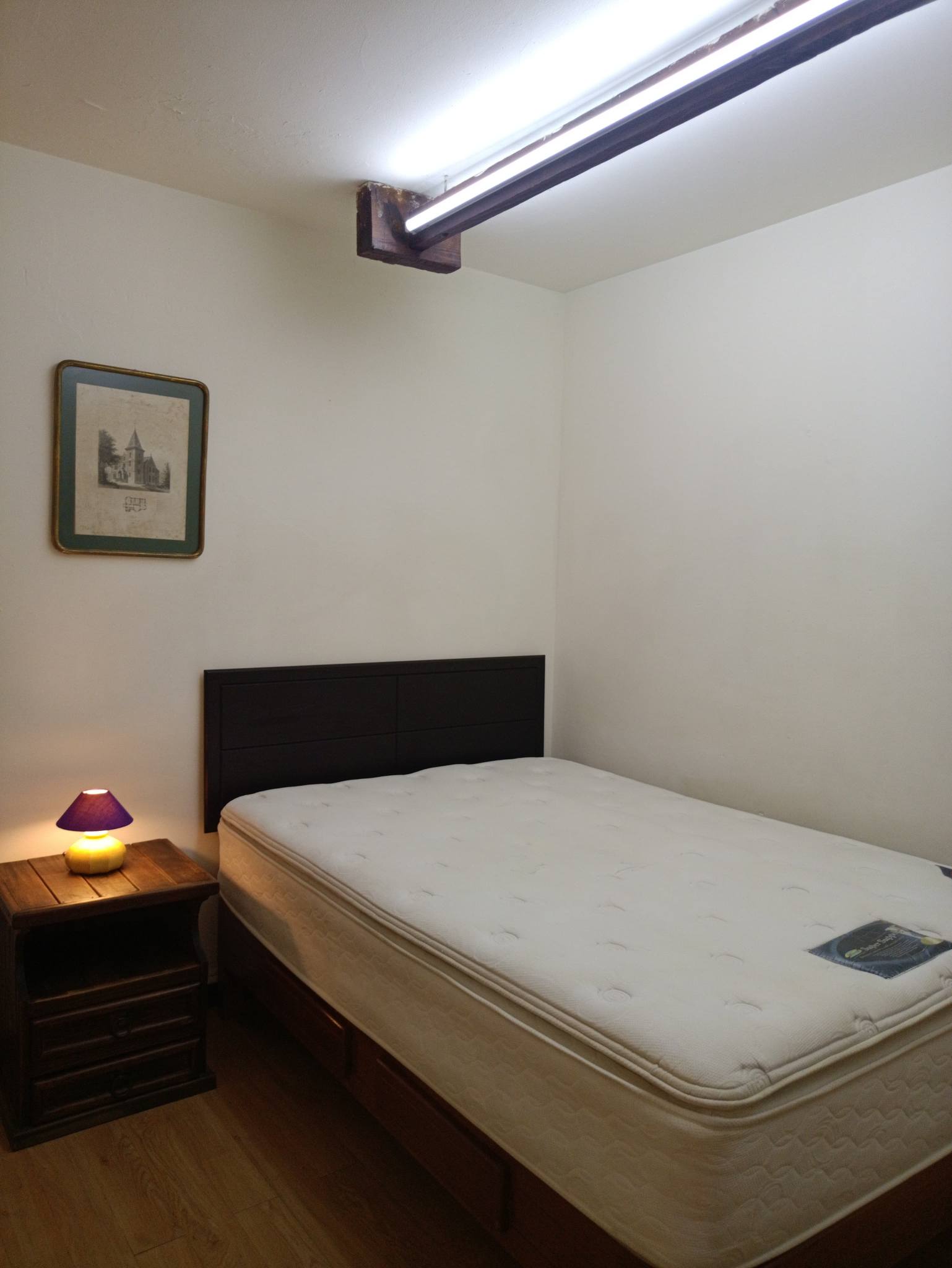 Recámara con cama, buró y iluminación adecuada.