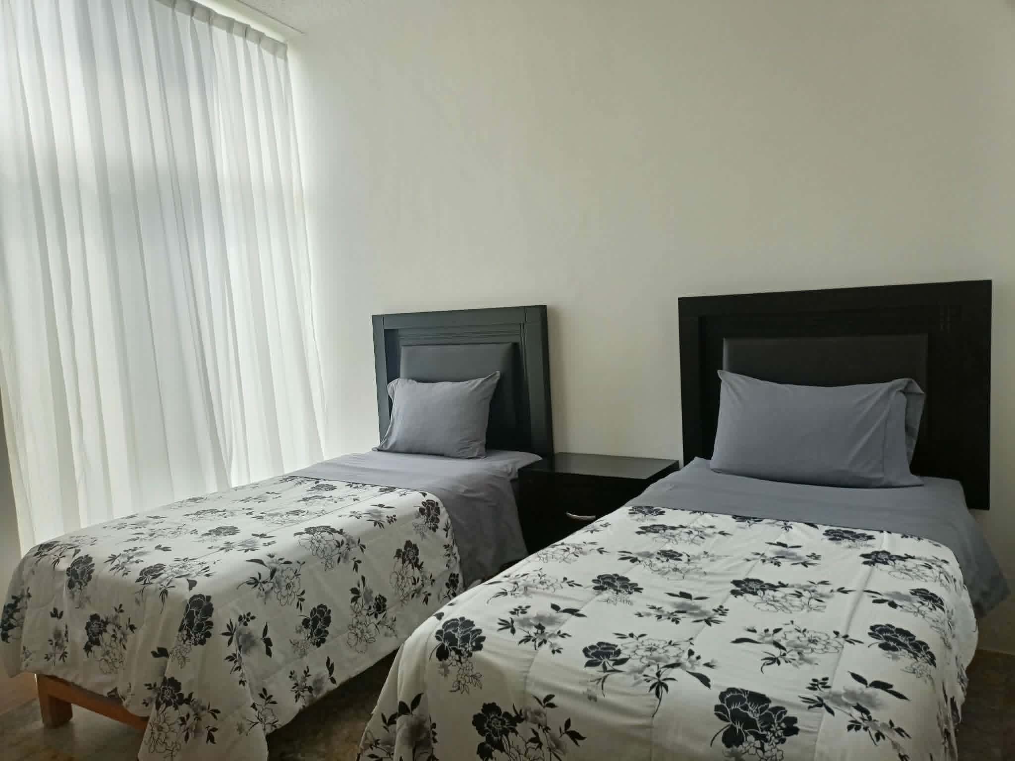 Habitación con camas individuales y decorado sencillo. Cortinas translúcidas.