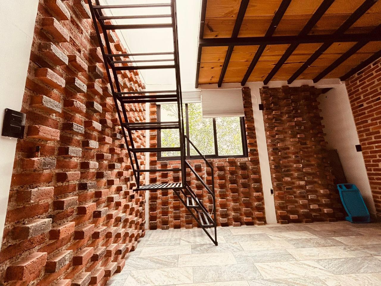 Sala con paredes de ladrillo y escalera de metal, conecta a la terraza y otras áreas.
